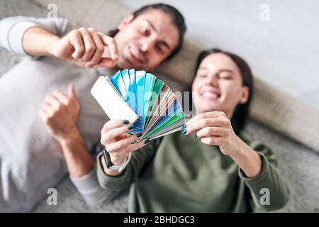 Mani di giovane donna che giace sul pavimento vicino al suo marito e tenendo tavolozza mentre consultandosi con lui circa la scelta del colore Foto Stock