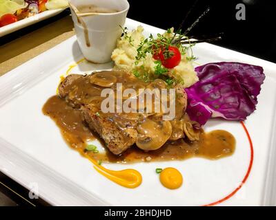 Foto di bistecca di maiale bianca con sugo e cavolo sul piatto bianco Foto Stock