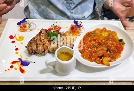 Foto di bistecca di maiale e sugo con il suo contorno sul piatto bianco e bella decorazione nel fast food di Bluport Hua Hin, Thailandia dicembre 28, Foto Stock