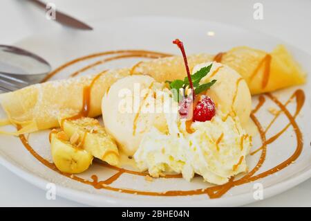 Gelato alla vaniglia e crepes farciti con banane ricoperte di caramello e panna montata. Foto Stock