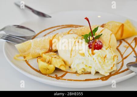 Gelato alla vaniglia e crepes farciti con banane ricoperte di caramello e panna montata. Foto Stock