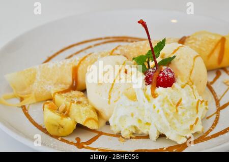 Gelato alla vaniglia e crepes farciti con banane ricoperte di caramello e panna montata. Foto Stock