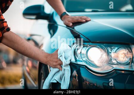 Primo piano, sparare di un maschio mani lucidare con cura la sua auto con un panno in microfibra, all'aperto. Foto Stock