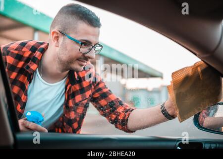 Giovane uomo che pulisce i vetri sulla sua automobile con panno di microfibra. Foto Stock