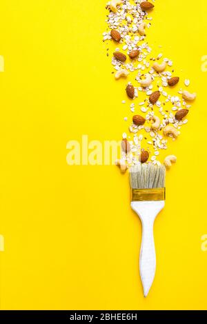 pennello con fiocchi di farina d'avena e mandorle isolato su sfondo giallo, spazio per la copia del testo Foto Stock