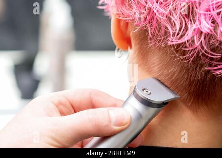 Vista posteriore parrucchiere mano è rasare capelli rosa di donna con rifinitore elettrico in salone di parrucchiere, primo piano. Foto Stock