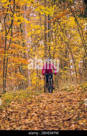 Bella donna anziana in sella alla sua bici elettrica sui sentieri autunnali della foresta vicino a Stoccarda, bellissimi colori caldi Foto Stock