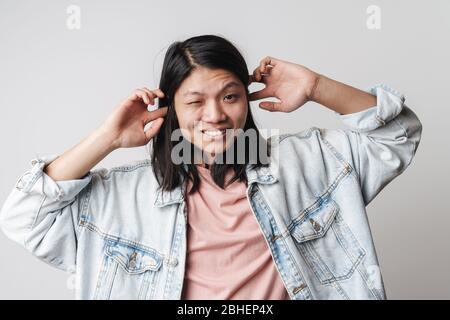 Ritratto di una giovane donna asiatica infastidita che indossa giacca in denim guardando la macchina fotografica isolata su sfondo bianco Foto Stock