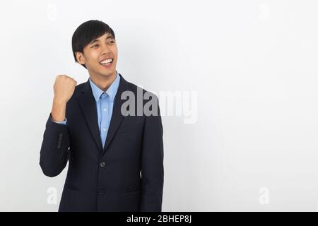 Eccitato giovane business asiatico uomo che alza i pugni con felice faccia felice, celebrando il successo isolato su sfondo bianco. Foto Stock