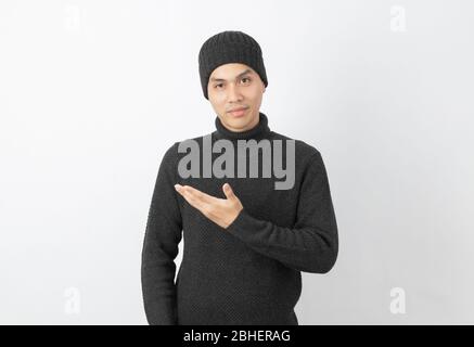 Giovane uomo asiatico bello che indossa maglione grigio e beanie che punta al lato con le mani per presentare un prodotto o un'idea su sfondo bianco. Foto Stock