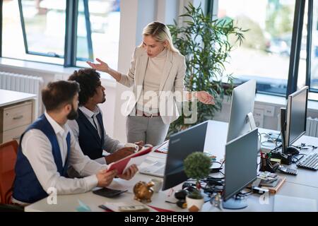 insoddisfatto bionda boss caucasica femmina che si chiede, spiegando e facendo domande a due colleghi maschi in ufficio Foto Stock
