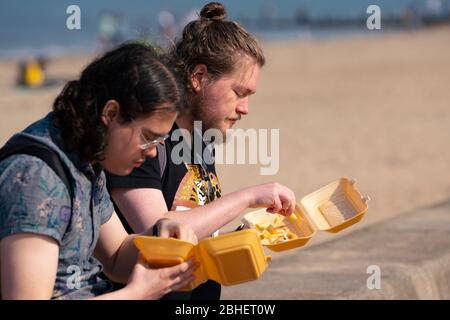 Portobello, Scozia, Regno Unito. 25 aprile 2020. Vista della gente all'aperto il sabato pomeriggio sulla spiaggia e sul lungomare di Portobello, Edimburgo. Il bel tempo ha portato più persone all'aperto a piedi e in bicicletta. La spiaggia sembra occupata con possibile un guasto nelle distanze sociali che accadono più tardi nel pomeriggio. La gente mangia patatine sul lungomare, una bancarella di cibo da asporto è aperta. Iain Masterton/Alamy Live News Foto Stock