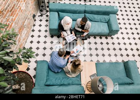 I viaggiatori d'affari si riunano e si riunano nella moderna sala d'ufficio loft. Partner multietnici che discutono di nuovi progetti utilizzando report finanziari, tablet e. Foto Stock