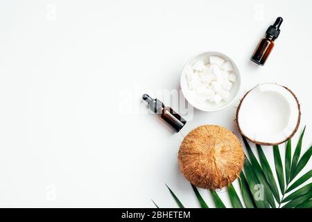 Olio essenziale di cocco naturale per la cura dei capelli con foglie di palma e noci di cocco su sfondo bianco. SPA biologico cosmetico, salute e bellezza concetto. Disposizione piatta Foto Stock