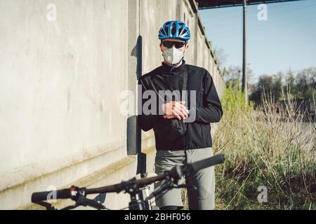 Ciclista in maschera facciale a causa di smog in città. Corriere della bici che fa una consegna. Uomo che indossa la maschera di coronavirus 19. Ciclista in maschera di inquinamento da Foto Stock