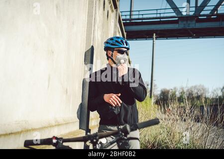 Ciclista in maschera facciale a causa di smog in città. Corriere della bici che fa una consegna. Uomo che indossa la maschera di coronavirus 19. Ciclista in maschera di inquinamento da Foto Stock