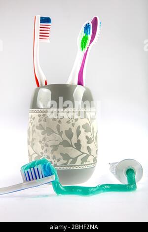 Dentifricio verde e spazzolini multicolore in un bicchiere speciale accanto a un tubo di dentifricio. Ancora vita. Foto Stock