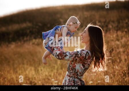 Bella donna solleva in alto la sua adorabile bambina a metà aria e guarda il suo sorriso. Buon genitore che spende il tempo che gioca con la figlia nel parco a. Foto Stock