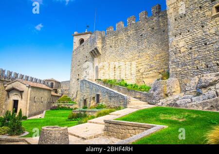 Repubblica San Marino, 18 settembre 2018: Cortile con prato verde erba di prima Torre Guaita prima torre medievale con mura in pietra con merli sulla roccia del Monte Titano con cielo blu Foto Stock