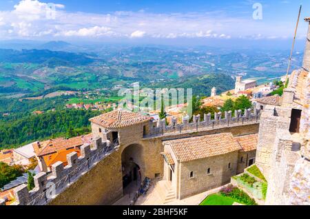 Repubblica San Marino, 18 settembre 2018: Veduta aerea del paesaggio con valle, colline verdi, campi, villaggi di quartiere suburbano, cielo blu sfondo e fortezza in pietra muro e torre con merli Foto Stock