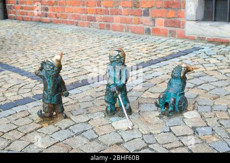 Wroclaw, Polonia, 7 maggio 2019: Tre nani: Sordi, ciechi con un bastone e invalidi in una sedia a rotelle, famoso gnomo in bronzo in miniatura con la scultura del cappello è un simbolo di Wroclaw nel centro storico della città vecchia Foto Stock