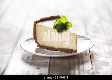 Fetta di cheesecake classica di New York con un rametto di menta su un piatto su un tavolo di legno. Il concetto di dolci e dolci dolci dessert Foto Stock
