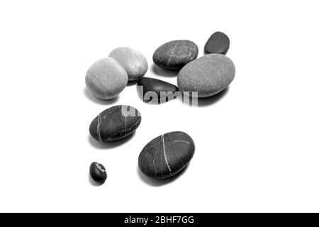 Ciottoli di mare sparsi. Mucchio di pietre nere e grigie lisce isolate su sfondo bianco Foto Stock