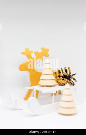 Renna giocattolo, slitta di Natale in legno, albero di natale e fiocchi di neve su uno sfondo bianco.decorazione di Natale con slitta in legno, cono di pino, regali Foto Stock