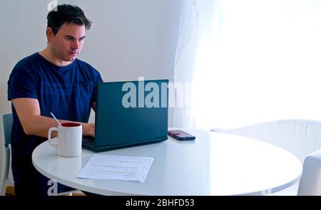Giovane uomo seduto e che lavora a casa con un notebook. Concetto di padre che lavora. Concetto di telelavoro . Foto Stock