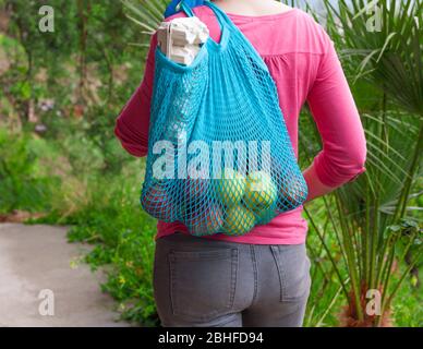 Donna in guanti tiene eco borsa stringa riempito con alimentari e verdure. Shopping durante le emergenze pandemiche, Covid-19 Foto Stock