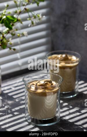 Dalgona caffè in bicchieri trasparenti su davanzale illuminato dalla luce del sole. Foto Stock