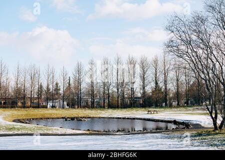 Un lago con un tavolo con panchine, in un parco innevato a Reykjavik, Islanda Foto Stock
