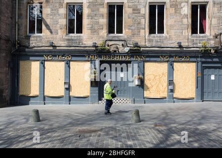 È il blocco di Coronavirus. Un operaio solista vaga davanti a un pub a bordo nel Grassmarket di Edimburgo. Foto Stock