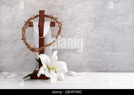 Composizione con corona di spine, croce di legno e giglio su fondo chiaro Foto Stock