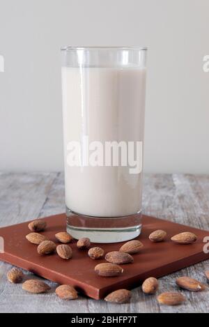 Bicchiere di latte di mandorla vegana su cotto circondato da mandorle Foto Stock