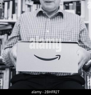 Parigi, Francia - 2 aprile 2019: Immagine quadrata bianca e nera Happy Senior man in soggiorno nuovo pacco consegnato da Amazon prime e-commerce Foto Stock