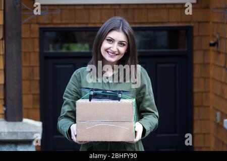 Bella giovane donna bruna sorridente che tiene un pacchetto che è stato consegnato da un drone autonomo. Foto Stock