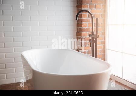 Bagno moderno con vasca bianca indipendente e rubinetto nero. Pareti in mattoni in stile loft Foto Stock