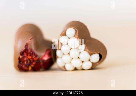 Due cioccolatini artigianali a forma di cuore con ripieno rosso e bianco giacciono sul tavolo in legno. Spazio di copia Foto Stock