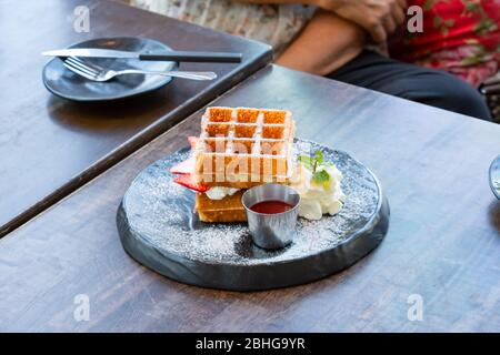 Waffle Strawerry panna fresca nella piastra nera su un tavolo di legno. Foto Stock