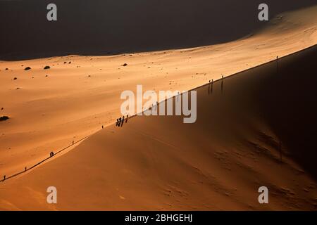 Persone che arrampicano sulle dune di sabbia accanto a Deadvlei, vicino a Sossusvlei, Namib-Naukluft National Park, Namibia, Africa Foto Stock