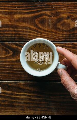 tazza di tè bianco con una mano su un tavolo di legno Foto Stock