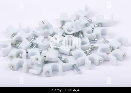 Primo piano di clip per cavi in plastica con chiodi in acciaio galvanizzato su sfondo bianco Foto Stock