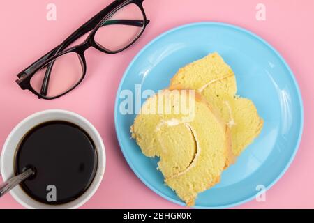 Occhiali da vista, fetta di torta svizzera e tazza di caffè su sfondo rosa. Concetto di pausa tè Foto Stock