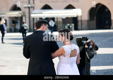 Praga, Repubblica Ceca - 23 aprile 2020: Coppia di nozze in maschere mediche viso fotografata da fotografo con maschera facciale nella città vecchia. Matrimonio durante la pandemia coronavirus. COVID-19 matrimoni. Foto Stock