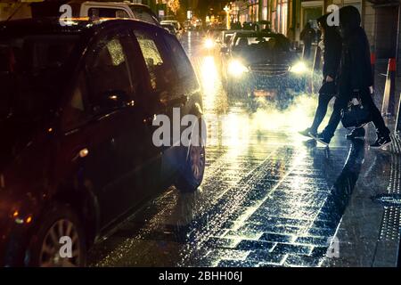Coppia nelle cappe attraversare la strada di notte sotto la pioggia Foto Stock