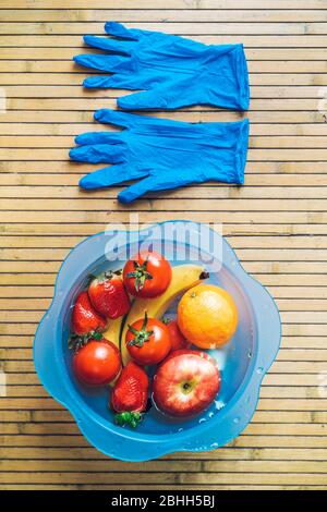 Ciotola blu con frutta fresca e pulita su una base di legno con guanti in lattice blu. Foto Stock