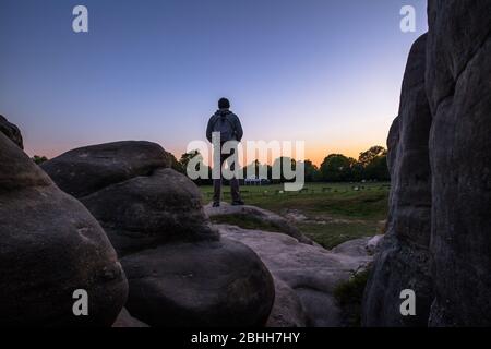 Wellington Rocks, Royal Tunbridge Wells, Kent uno sperone roccioso naturale di arenaria sul comune, uomo con zaino in piedi sul tramonto di osservazione della roccia Foto Stock