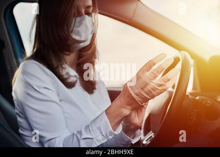 Donna indossa la maschera protettiva e i guanti di medicina prima di guidare in auto. Concetto di protezione del coronavirus covid-19 Foto Stock