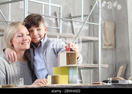 Madre felice e figlio che gioca a costruire una casa con modelli di costruzione in cantiere. Casa acquistare e costruire obiettivo concetto Foto Stock